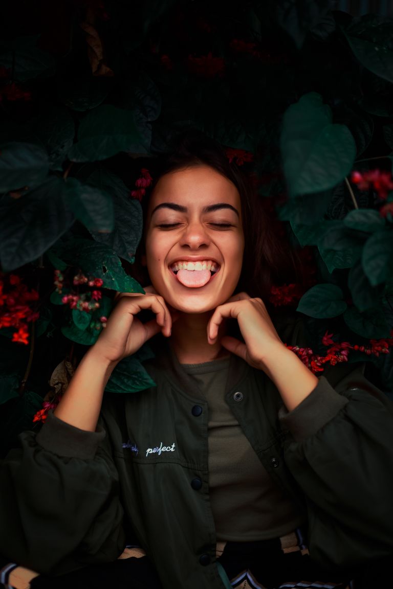 Joyful woman with eyes closed and tongue out surrounded by dark green leaves.