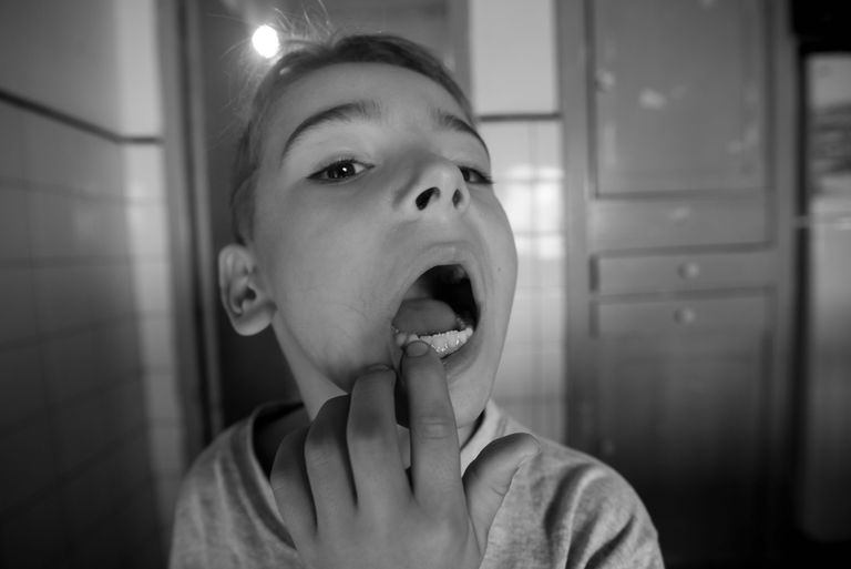 A child examining their own open mouth in a black and white indoor setting.